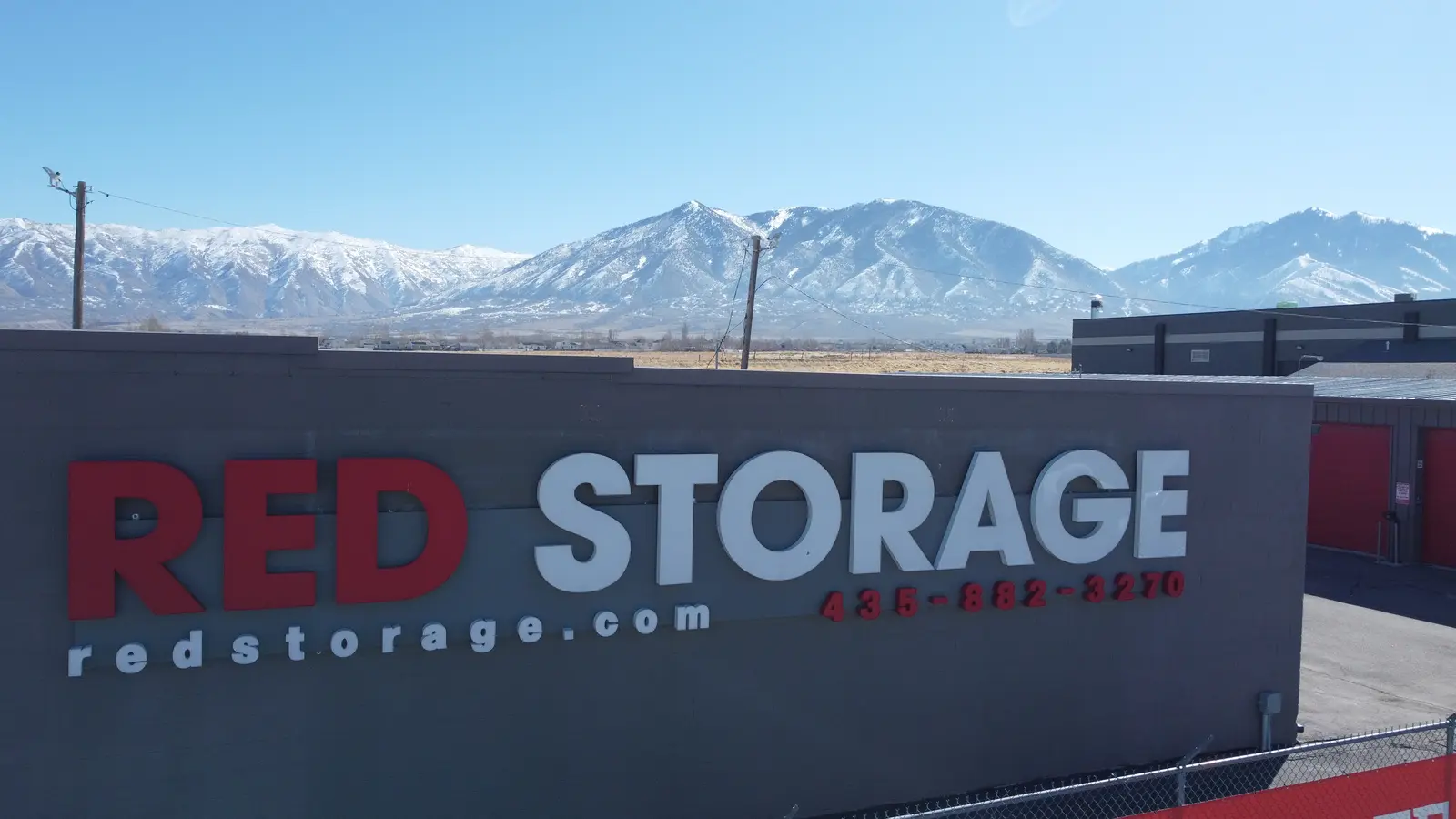 Red Storage branded metal self-storage building against snowcapped mountains, Tooele UT